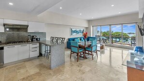 A modern kitchen with granite countertops, white cabinets, and a dining area with blue chairs and a table. - 4BR Marina Ocean-View Above Casino 2 Suites (Puerto Vallarta)