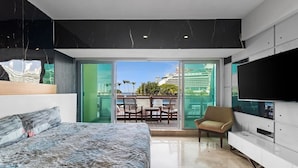 A modern bedroom with a bed, a TV, and a balcony with a view of a cruise ship and buildings. - 4BR Marina Ocean-View Above Casino 2 Suites (Puerto Vallarta)