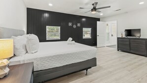 Un dormitorio moderno con una cama, mesita de noche, ventilador de techo y televisor sobre un aparador.