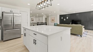 Una cocina moderna con una isla grande, electrodomésticos de acero inoxidable y un comedor con una pared de acento negra y un televisor de pantalla plana.