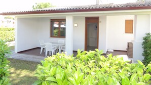 A single-story house with a tiled roof, a small porch with a table and chairs, and a door leading to an interior room. - Terraced Villa With Garden and Pools (San Michele al Tagliamento)