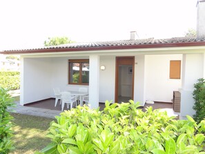 A single-story house with a tiled roof, a small porch with a table and chairs, and a door leading to an interior room. - Terraced Villa With Garden and Pools (San Michele al Tagliamento)