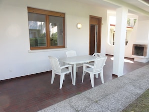 Een terras met een witte tafel en stoelen, een bakstenen open haard en een raam met houten kader.