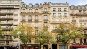 Una hilera de edificios de varios pisos con balcones, locales comerciales y una señalización de estacionamiento visible.