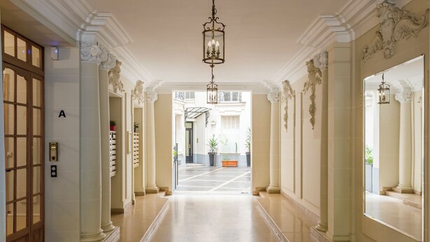 Un amplio pasillo con columnas ornamentadas, un candelabro y vista al exterior del edificio.