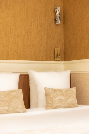A hotel room with a wooden headboard, a wall-mounted light fixture, and a bed with white bedding and patterned pillows. - Luxury Suite - Wagram (Paris)