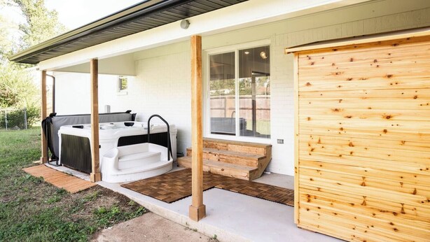 Un patio couvert avec un jacuzzi, des marches en bois menant à un garage et un mur extérieur blanc.