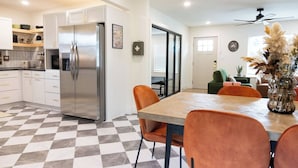 Une cuisine moderne avec un réfrigérateur en acier inoxydable, un coin repas doté d’un sol à carreaux et un salon avec un canapé vert et un vase de fleurs.