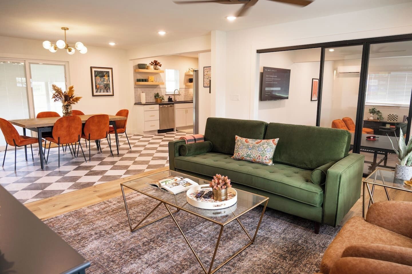 Ein modernes Wohnzimmer mit einem grünen Sofa, orangefarbenen Sesseln, einem Couchtisch und einem karierten Boden.
