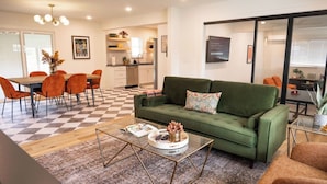 Un salon moderne avec un canapé vert, des fauteuils orange, une table basse et un sol à carreaux.