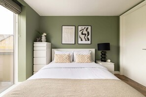 A bedroom with a bed, two wall art pieces, a nightstand with a lamp, and a dresser.