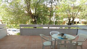 A terrace with a table and chairs, a railing, and a view of trees and buildings. - Cozy Apartment With Private Entrance (San Michele al Tagliamento)