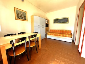 Une pièce de taille modeste, avec une table et des chaises en bois, un canapé, un meuble et deux tableaux encadrés accrochés aux murs.