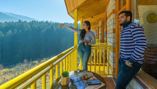 Een houten balkon met een gele railing met uitzicht op een bebost dal.