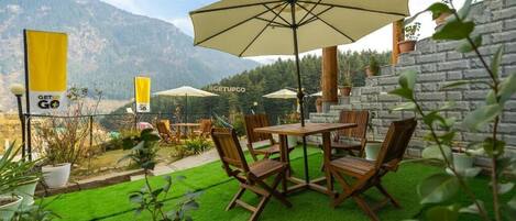 An outdoor patio with a wooden table and chairs, surrounded by potted plants and a stone wall.