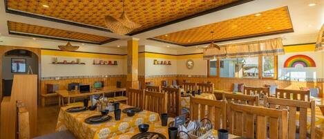 Un restaurante con manteles amarillos estampados, sillas de madera y un techo con diseño floral.