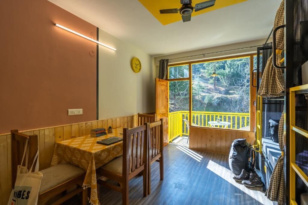 Una habitación acogedora con una mesa y sillas de madera, un banco, un ventanal con vistas a árboles y un ventilador de techo.