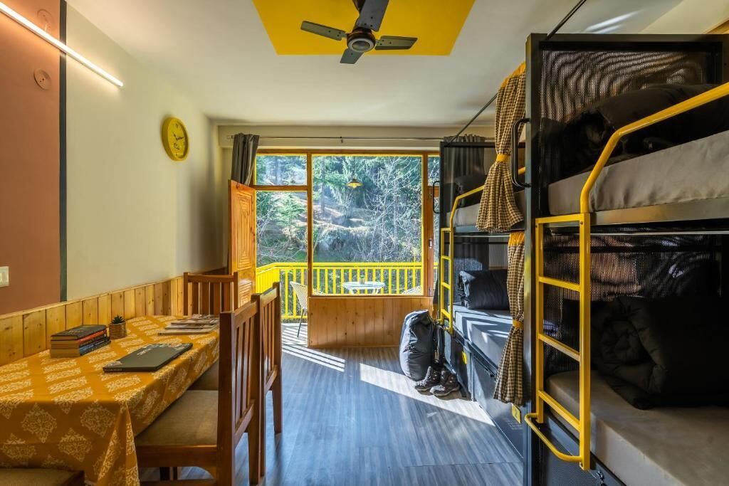 A compact room with bunk beds, a small table with books, a chair, and a window with a view of trees.