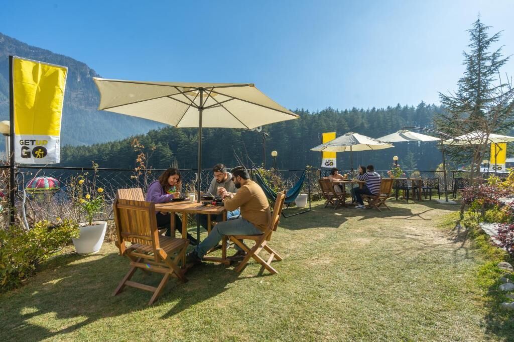 An outdoor seating area with tables and chairs, surrounded by a fence and potted plants.