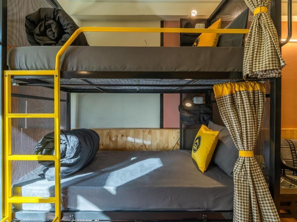 Un lit superposé avec une échelle, une petite table et un rideau.