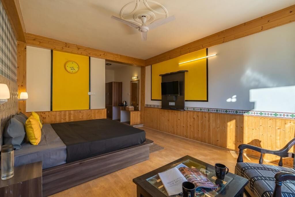 A room with a bed, a sofa, a coffee table, a TV, and a wooden wall with a clock.