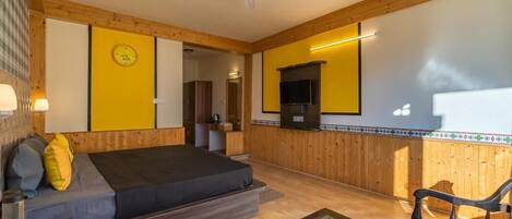 A room with a bed, a sofa, a coffee table, a TV, and a wooden wall with a clock.