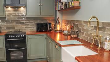 A kitchen with a stove, microwave, and a sink with a wooden countertop.
