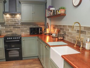 A kitchen with a stove, microwave, and a sink with a wooden countertop. - Robins Rest at The Lodge (Kilmacthomas)