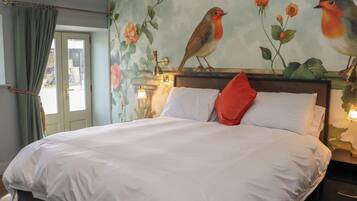 A bed with white linens, a red pillow, and a wall mural of birds and flowers.