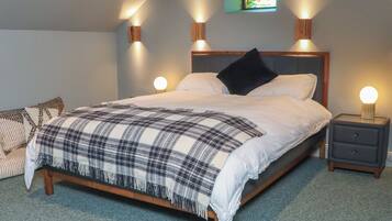 A bedroom with a bed, two bedside tables, a nightstand, a wall-mounted light, and a small window.