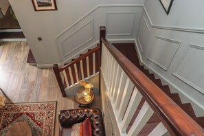 A staircase with a wooden handrail and white balusters, a patterned rug, and a leather bench with a cushion. - Robins Rest at The Lodge (Kilmacthomas)