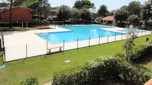 A rectangular swimming pool with a white deck and a fence. - Apartment With Garden and Pool Access (San Michele al Tagliamento)