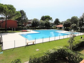 A rectangular swimming pool with a white deck and a fence. - Apartment With Garden and Pool Access (San Michele al Tagliamento)