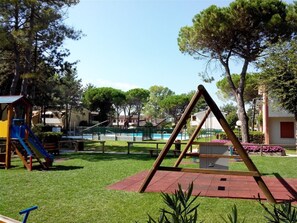 Un parque infantil con columpios, un tobogán y una piscina pequeña.