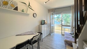 A modern living space with a dining area, a sofa, a TV, and a balcony with a view. - Bright Duplex Apartment Near Beach (San Michele al Tagliamento)