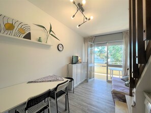 A modern living space with a dining area, a sofa, a TV, and a balcony with a view. - Bright Duplex Apartment Near Beach (San Michele al Tagliamento)