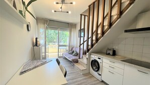 A compact kitchen with a washing machine, a dining area with a table and chairs, and a staircase leading to a balcony. - Bright Duplex Apartment Near Beach (San Michele al Tagliamento)