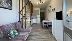 A compact living space with a sofa, a dining table, a kitchen area, and a staircase. - Bright Duplex Apartment Near Beach (San Michele al Tagliamento)