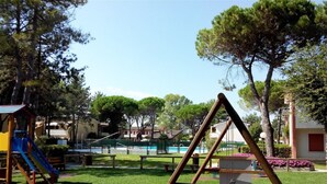 A playground with a swing set, a slide, and a small pool. - Bibione Apartment With Pool Access (San Michele al Tagliamento)