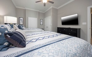 Une chambre à coucher avec un lit, une télévision, un ventilateur de plafond et une commode.