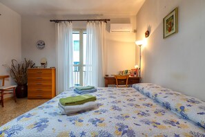 Une chambre à coucher comprenant un lit, une commode, un bureau, une chaise, une plante en pot et une fenêtre avec des rideaux.