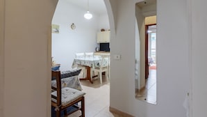 An arched doorway leading to a dining area with a table and chairs, a sofa, and a mirror on the wall. - Piera's Apartment In Alghero – Steps from the Seafront, Ideal for Couples and Families (Alghero)