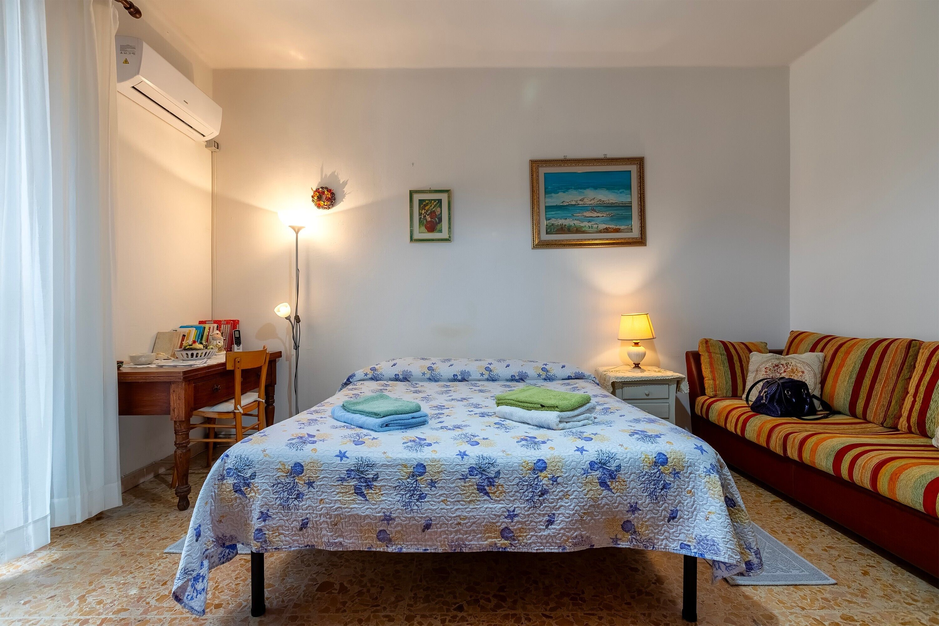 Une chambre à coucher comprenant un lit, un bureau, une chaise, un canapé, une lampe et un tableau accroché au mur.