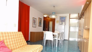 Un salon avec un canapé, une table à manger avec des chaises, un coin cuisine avec des placards et un rideau rouge.
