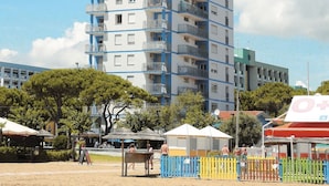 Un immeuble à plusieurs étages doté de balcons, avec un sol sablonneux et quelques arbres.