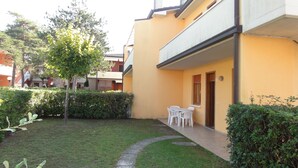 A courtyard with a small lawn, a tree, and a building with a balcony. - Apartment in a House With Garden (San Michele al Tagliamento)
