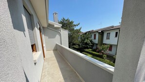 A narrow balcony with a tiled floor, white walls, and a view of neighboring houses and greenery. - Comfy Flat With Pool in Bibione (San Michele al Tagliamento)