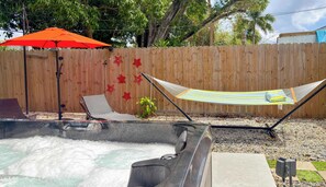 A hot tub with a wooden fence, a hammock, and a red umbrella in a backyard. - After Hours - Wilton Drive and Jacuzzi (Wilton Manors)