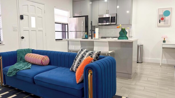 A modern kitchen with stainless steel appliances, a blue sofa with patterned cushions, and a small island with a microwave. - After Hours - Wilton Drive and Jacuzzi (Wilton Manors)