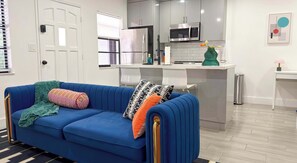 A modern kitchen with stainless steel appliances, a blue sofa with patterned cushions, and a small island with a microwave. - After Hours - Wilton Drive and Jacuzzi (Wilton Manors)